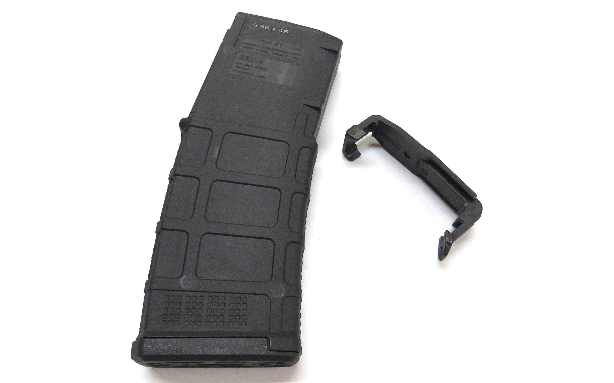 A black rifle magazine is lying on a white surface next to a detachable black cover or dust cap.