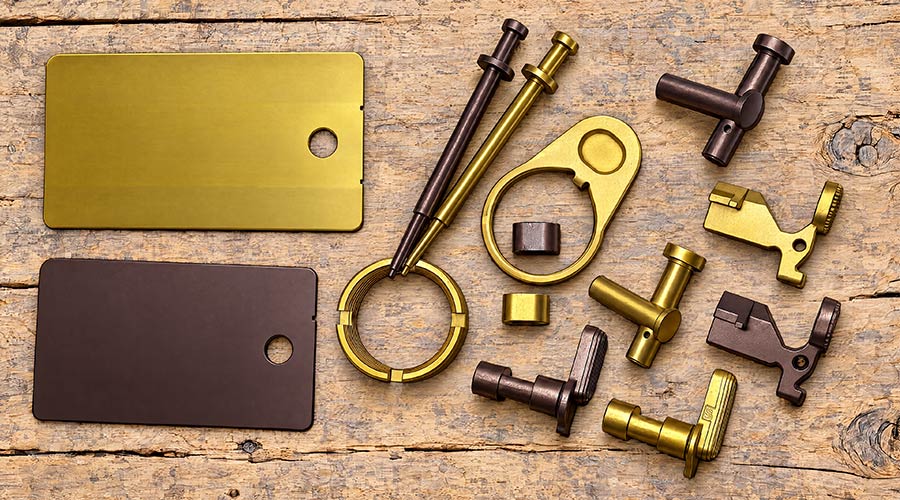 Brass and bronze metal hardware parts, including key rings, tags, and mechanical pieces, are arranged on a rustic wooden surface.